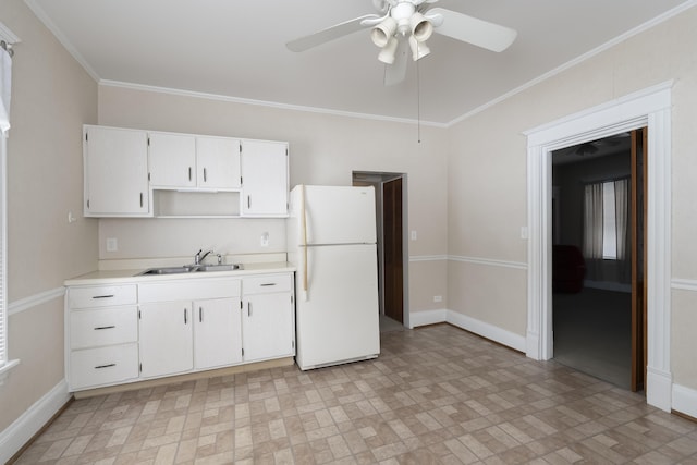 kitchen with light countertops, freestanding refrigerator, white cabinetry, a sink, and baseboards