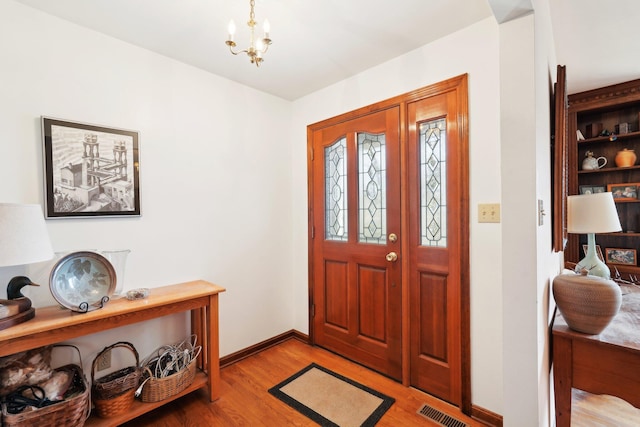 entrance foyer with light wood-type flooring, visible vents, baseboards, and an inviting chandelier