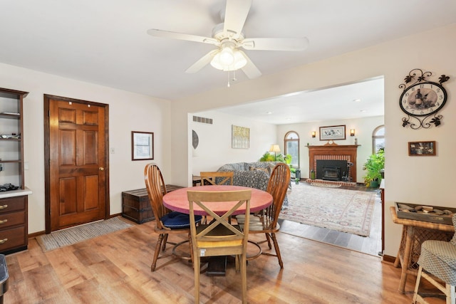 dining area featuring light wood-style flooring, a fireplace, visible vents, baseboards, and a ceiling fan