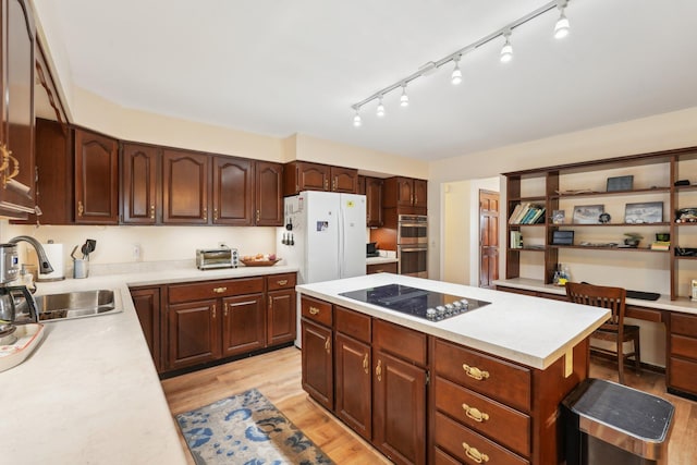 kitchen with black electric stovetop, light countertops, freestanding refrigerator, a sink, and light wood-type flooring