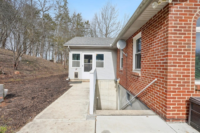 view of exterior entry with brick siding and a shingled roof