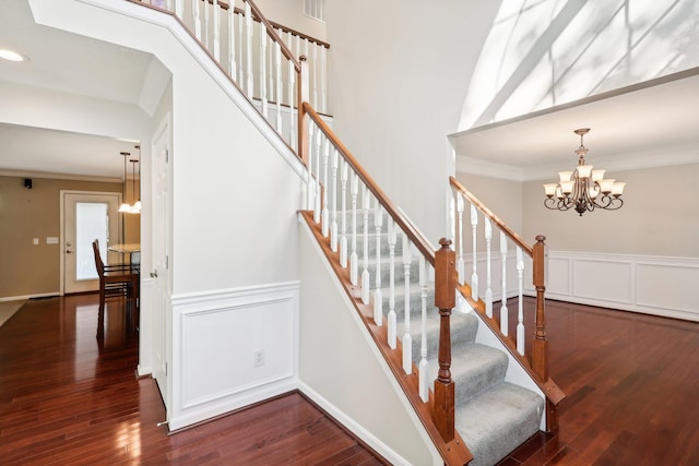 stairs featuring an inviting chandelier, wood finished floors, crown molding, and a decorative wall