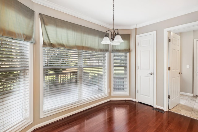 unfurnished dining area featuring a chandelier, baseboards, wood finished floors, and crown molding