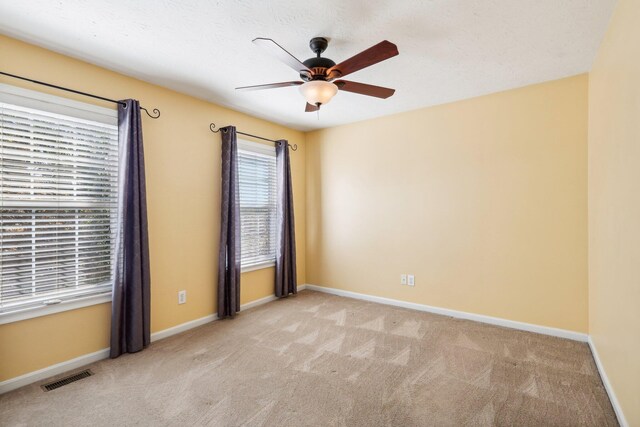 carpeted spare room with visible vents, ceiling fan, and baseboards