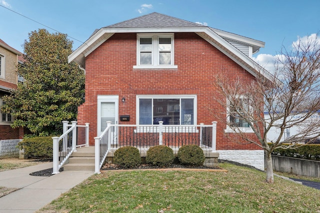 view of front of house featuring covered porch, brick siding, roof with shingles, and a front yard