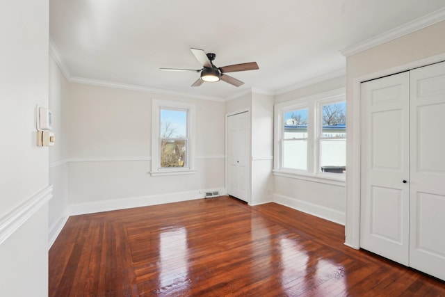 unfurnished bedroom featuring visible vents, baseboards, multiple closets, hardwood / wood-style floors, and crown molding