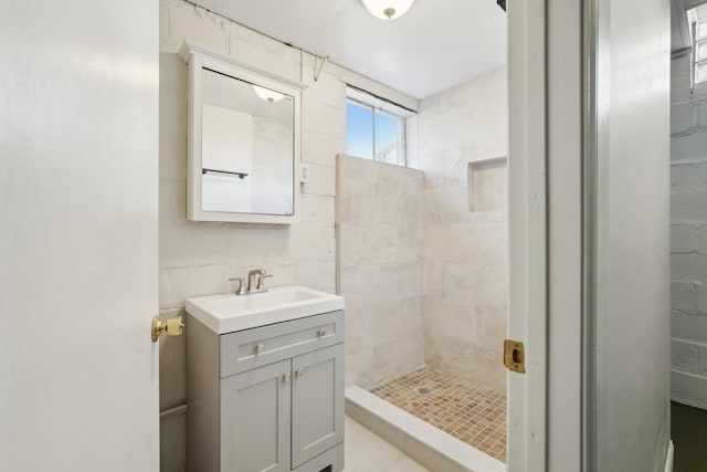 full bathroom with tile walls, tiled shower, and vanity