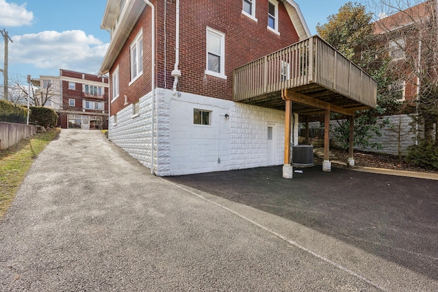 view of side of property featuring aphalt driveway, cooling unit, and brick siding