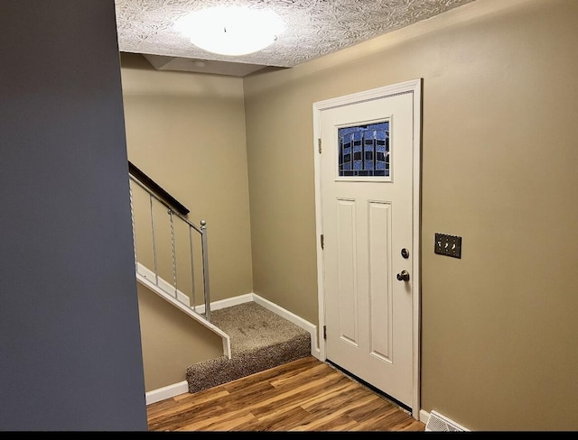 entryway featuring a textured ceiling, stairway, wood finished floors, and baseboards