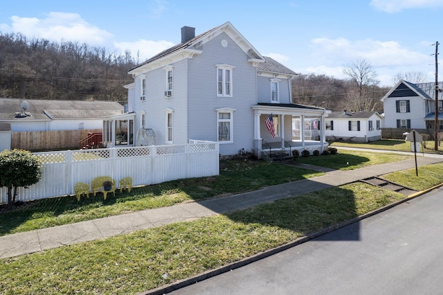 view of front of home featuring covered porch, a fenced front yard, a chimney, and a front lawn