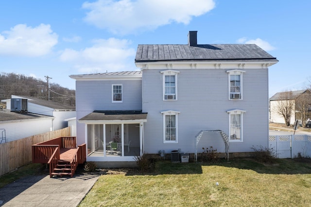 rear view of house featuring fence, a sunroom, a lawn, a standing seam roof, and a chimney