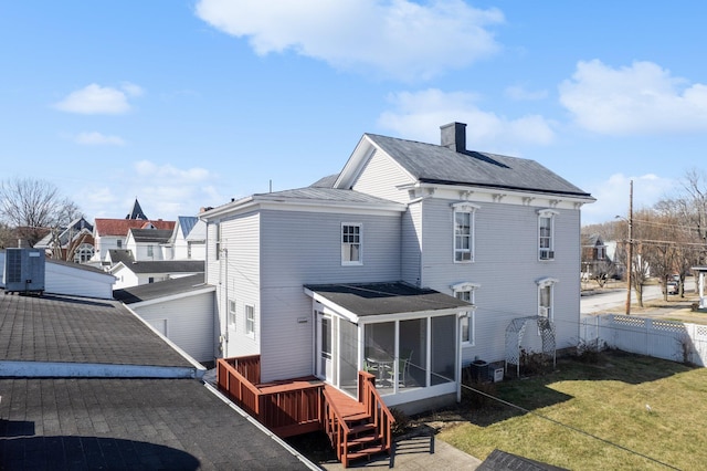 back of house featuring fence, a sunroom, a lawn, a wooden deck, and a chimney