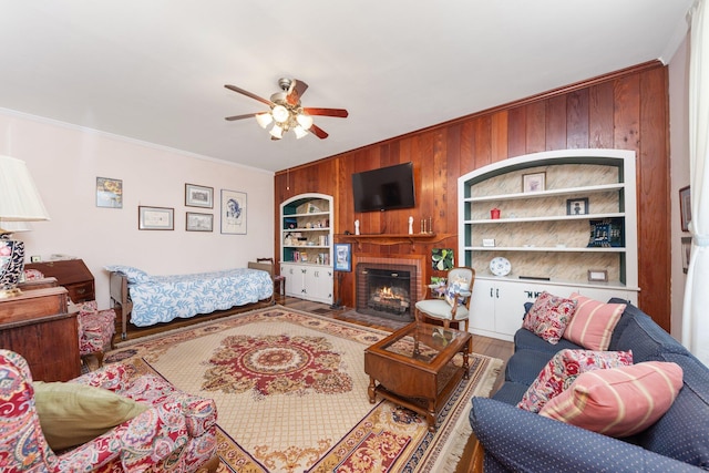 living area featuring a ceiling fan, ornamental molding, wood finished floors, wood walls, and a brick fireplace