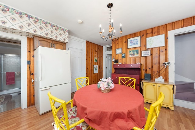 dining space with a chandelier, wood walls, and light wood-type flooring