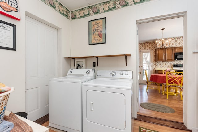 clothes washing area featuring wallpapered walls, laundry area, light wood finished floors, washer and dryer, and a notable chandelier