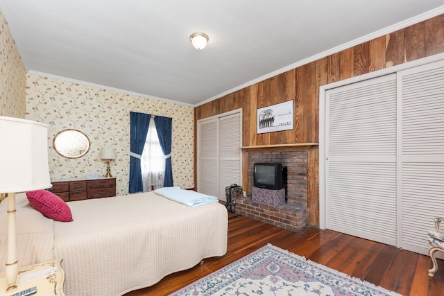 bedroom with wallpapered walls, ornamental molding, multiple closets, and wood finished floors