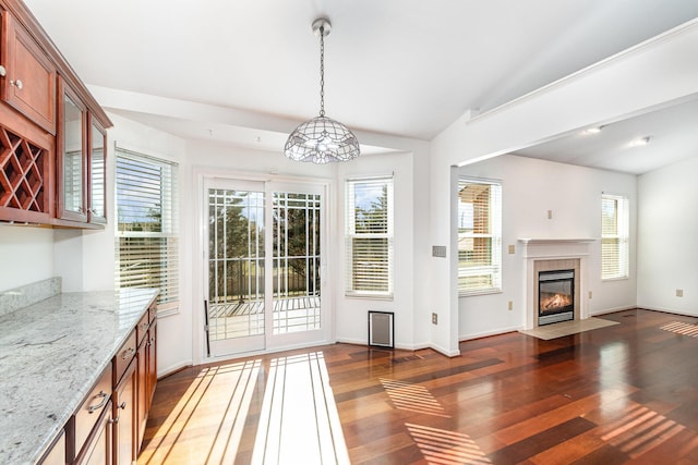 unfurnished dining area with a fireplace with flush hearth, baseboards, lofted ceiling, and wood finished floors