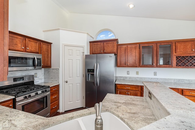 kitchen featuring light stone countertops, a sink, glass insert cabinets, appliances with stainless steel finishes, and backsplash