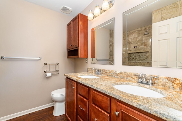 bathroom with double vanity, tiled shower, baseboards, and a sink