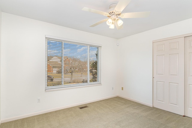 unfurnished bedroom featuring visible vents, baseboards, light colored carpet, a closet, and a ceiling fan