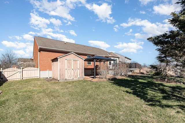 rear view of property featuring brick siding, a lawn, a storage shed, a fenced backyard, and an outbuilding