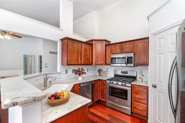 kitchen with dark wood-style floors, a peninsula, a sink, appliances with stainless steel finishes, and backsplash