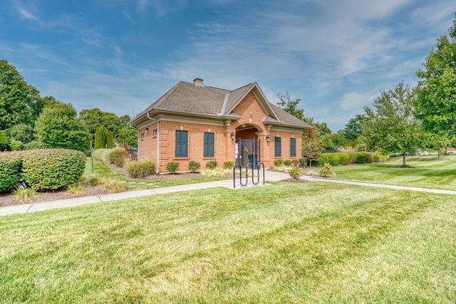 view of front of home with a front lawn, brick siding, roof with shingles, and a chimney