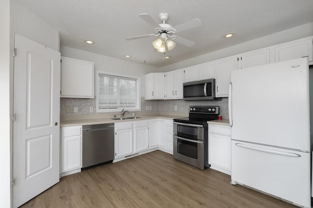 kitchen with light countertops, appliances with stainless steel finishes, white cabinets, a sink, and light wood-type flooring