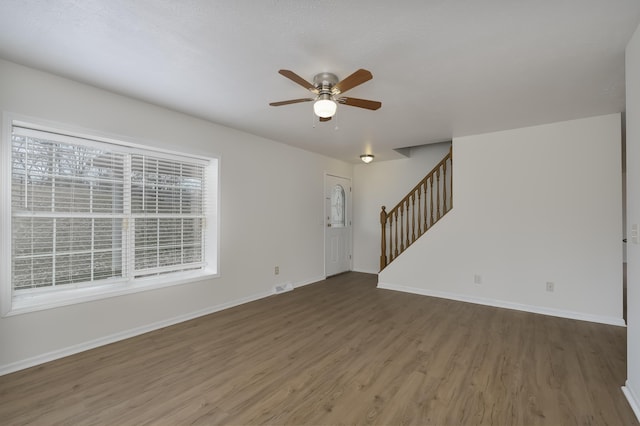 unfurnished living room featuring baseboards, visible vents, ceiling fan, stairway, and wood finished floors