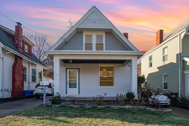 view of front of house with a porch, a lawn, and a chimney