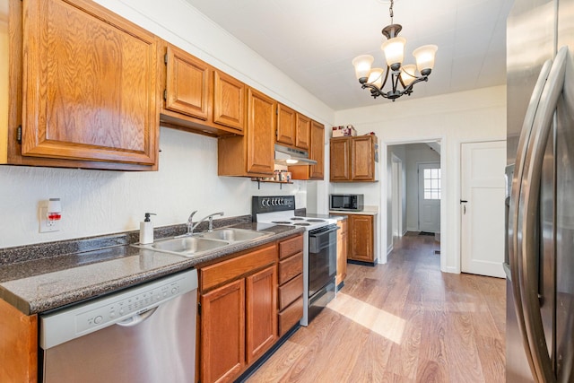 kitchen with under cabinet range hood, stainless steel appliances, a sink, light wood finished floors, and dark countertops