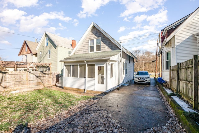 rear view of property with driveway, a sunroom, and fence