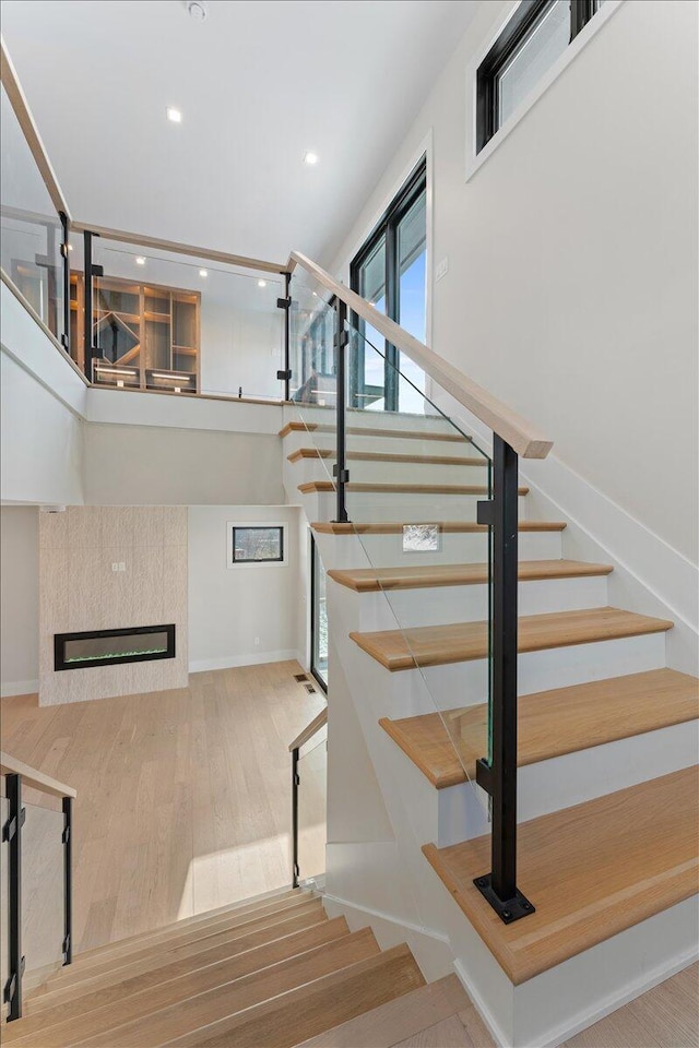 staircase featuring a tile fireplace, recessed lighting, baseboards, and wood finished floors