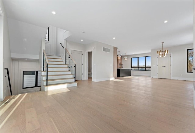 unfurnished living room featuring light wood finished floors, visible vents, an inviting chandelier, stairs, and a fireplace