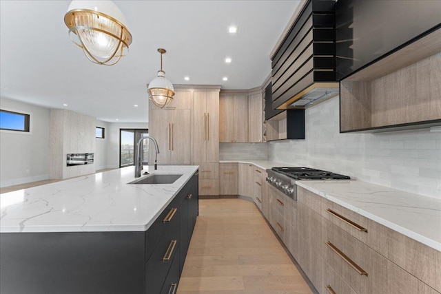 kitchen featuring modern cabinets, a large island with sink, light brown cabinetry, stainless steel gas stovetop, and a sink