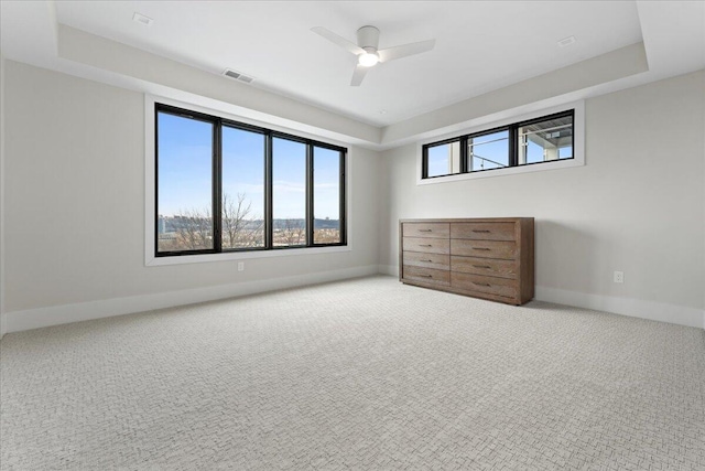 unfurnished bedroom with carpet floors, multiple windows, and a tray ceiling