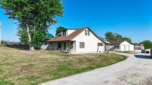 rear view of property featuring an outbuilding, fence, driveway, covered porch, and a lawn