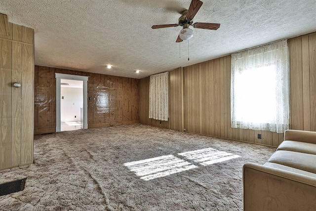 carpeted living area with wooden walls, a ceiling fan, and a textured ceiling