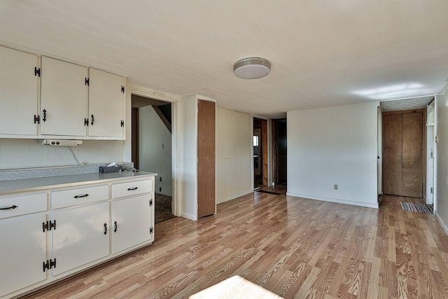 kitchen with baseboards, light wood finished floors, light countertops, white cabinets, and open floor plan