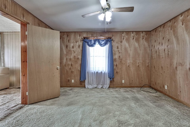 carpeted empty room featuring wooden walls, baseboards, and a ceiling fan