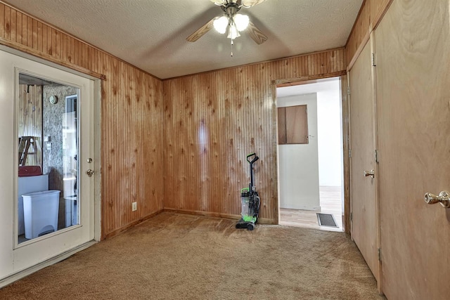 carpeted spare room with ceiling fan, visible vents, wood walls, and a textured ceiling