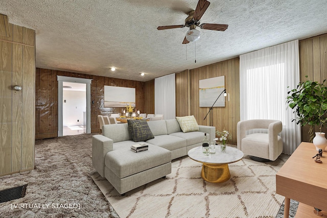 living area featuring ceiling fan, carpet flooring, a textured ceiling, and wooden walls