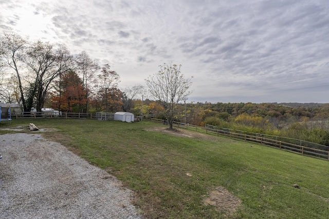 view of yard featuring a storage unit, fence, a wooded view, a rural view, and an outdoor structure