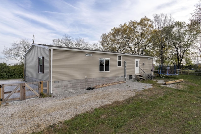 back of house with a trampoline, a lawn, entry steps, a gate, and crawl space