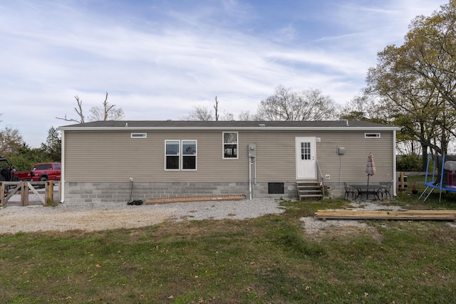 rear view of house featuring entry steps, crawl space, a trampoline, and a lawn