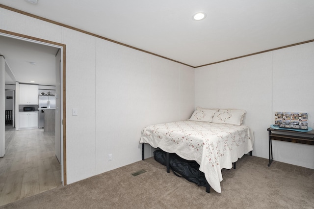 bedroom with light carpet, freestanding refrigerator, ornamental molding, and visible vents