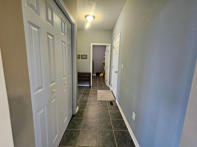 corridor featuring baseboards, a textured ceiling, and dark tile patterned flooring