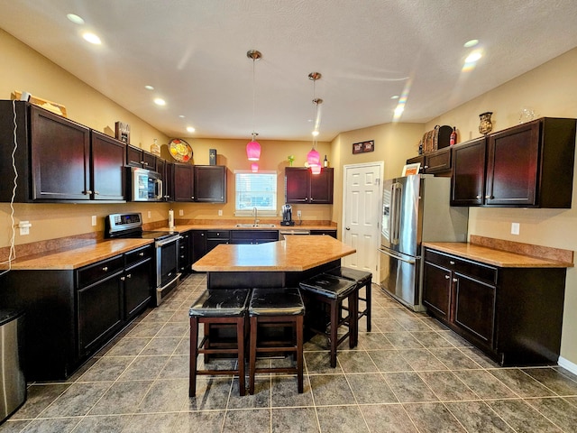 kitchen with a breakfast bar, stainless steel appliances, light countertops, a kitchen island, and a sink