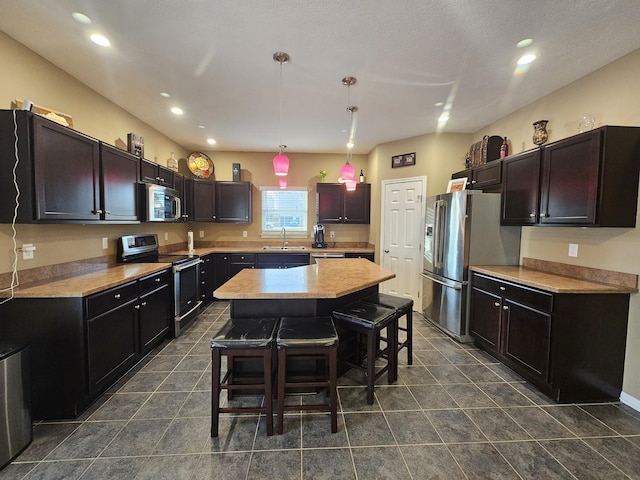 kitchen featuring a breakfast bar area, stainless steel appliances, hanging light fixtures, a sink, and a kitchen island