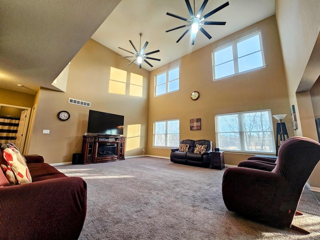 carpeted living area featuring ceiling fan, a glass covered fireplace, visible vents, and baseboards